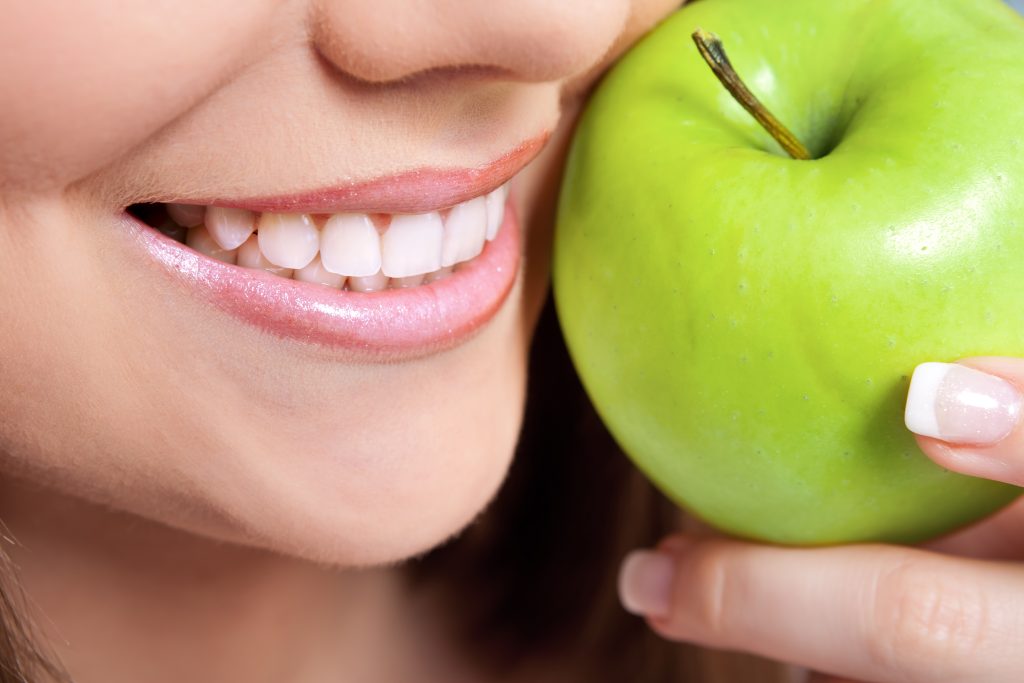 lady smiling with healthy teeth and green apple, close up