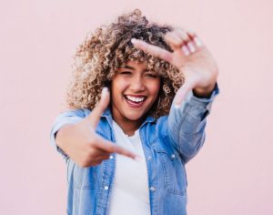 portrait of beautiful hispanic woman afro hair outdoors in spring doing frame with hands. pink wall